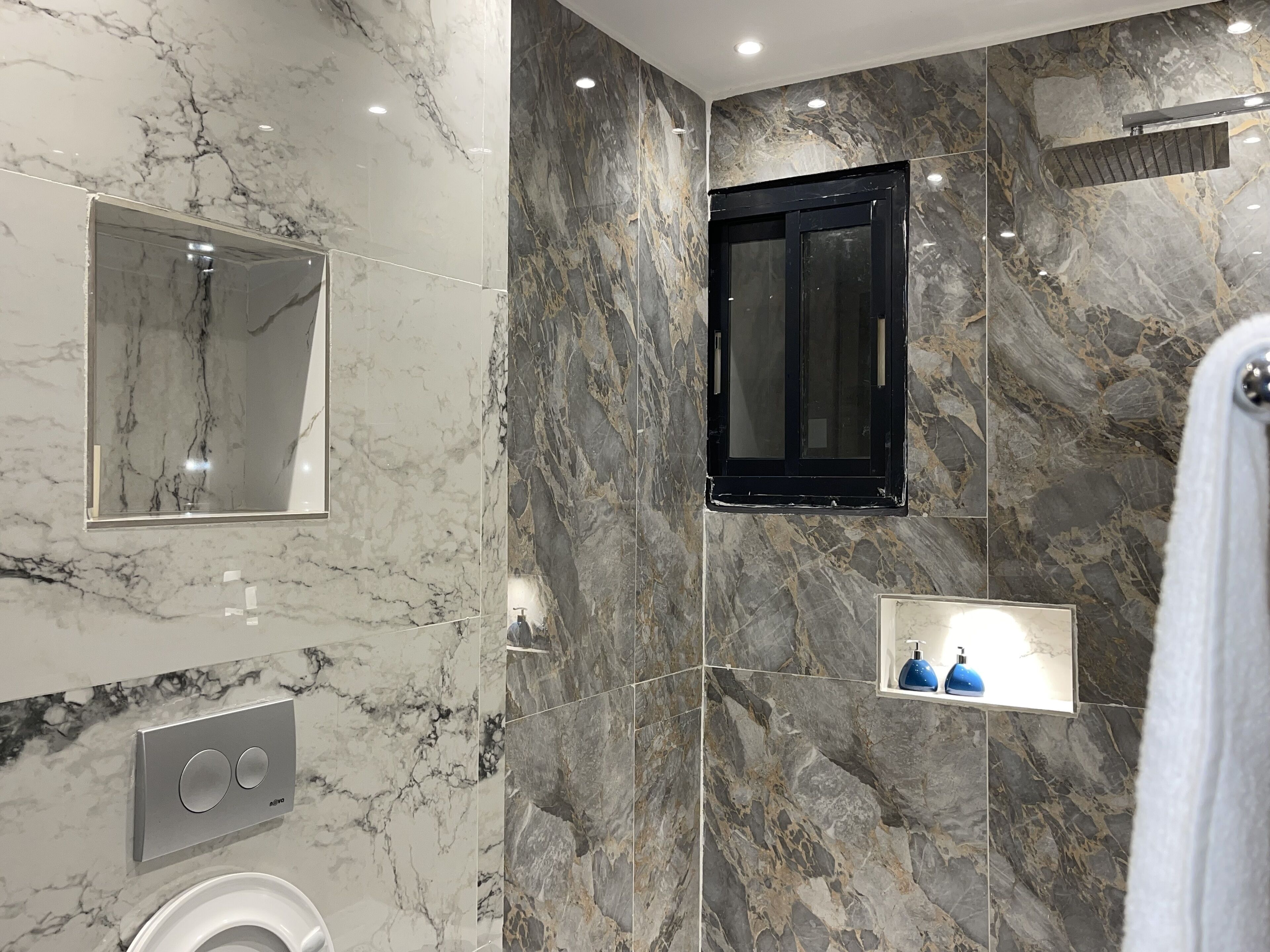 Un baño moderno con paredes de mármol, televisión integrada, toallero y panel de control.