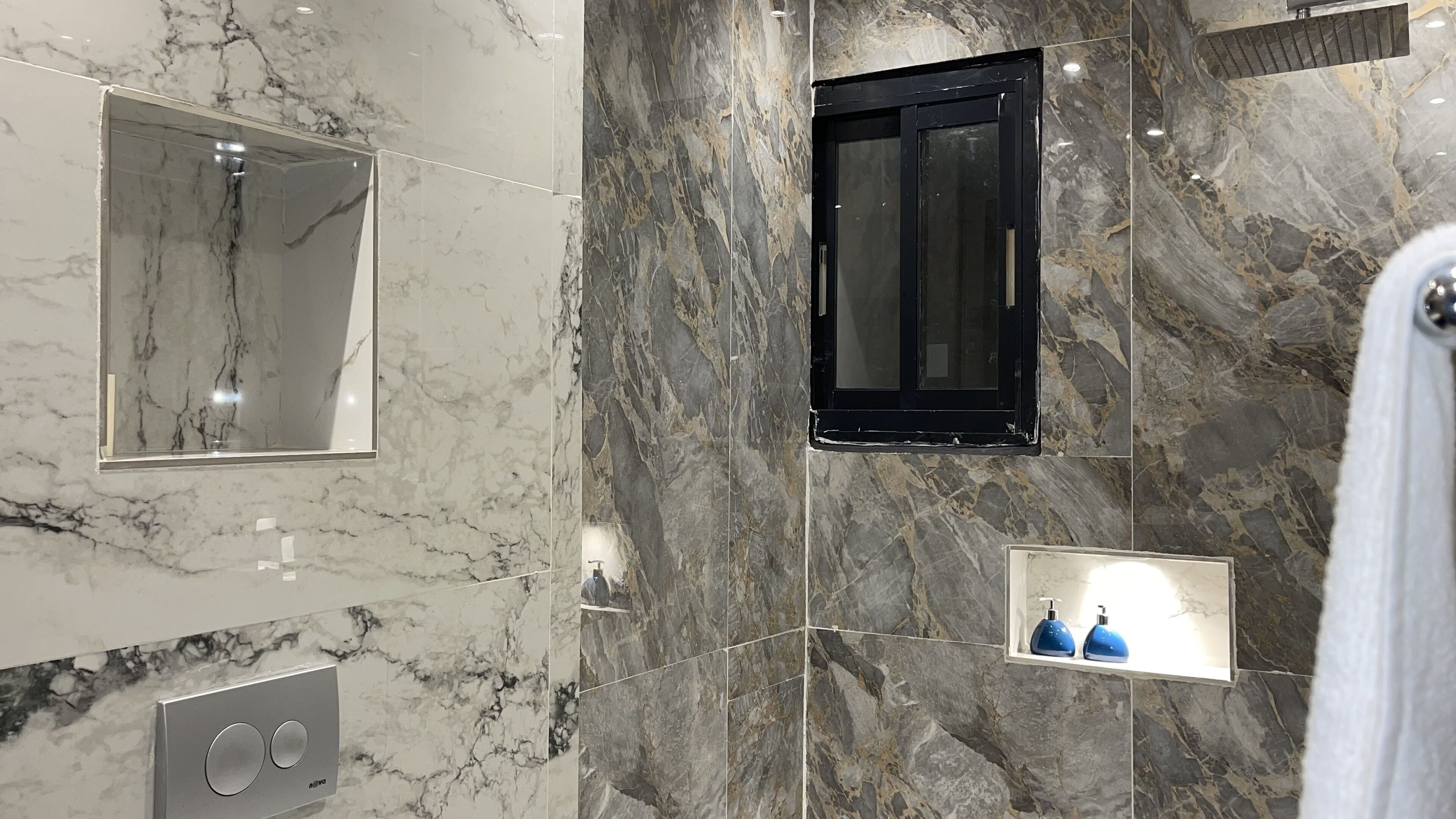 A bathroom with marble walls, a black-framed mirror, a built-in sink, and a towel rack.