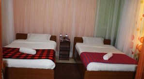 A hotel room with two single beds, each with a red and black checkered bedspread and a white pillow. There is a small table with two water bottles and glasses between the beds. - Hotel Kepler (Nairobi)