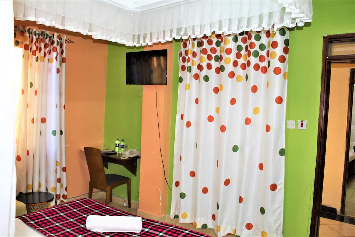 A room with a bed, a desk, a chair, a TV, and curtains with polka dots.