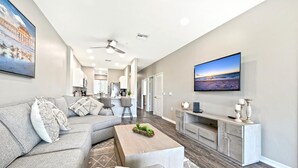 A modern living room with a grey sofa, a coffee table, and a TV on a stand. - GreenLinks at Lely Resort · King Bed · Lake View · Golf · Sleeps 6 (Naples)