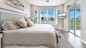 A bedroom with a large bed, a ceiling fan, a TV, and a view of the outdoors. - GreenLinks at Lely Resort · King Bed · Lake View · Golf · Sleeps 6 (Naples)