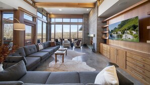 A spacious living room with a large sectional sofa, a flat-screen TV mounted on the wall, and a stone fireplace. - Corporate*Hot Tub•20 Acres•King Beds•Firepit•Views (Grove)