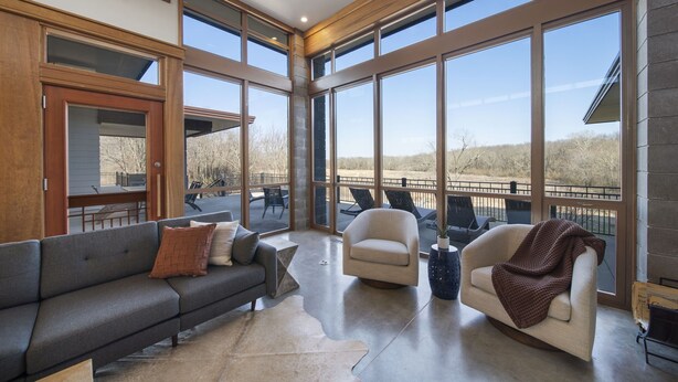 A spacious living area with a gray sofa, a beige armchair, and a coffee table. Large windows provide a view of the outdoors. - Corporate*Hot Tub•20 Acres•King Beds•Firepit•Views (Grove)