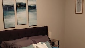 Un dormitorio con cama, mesita de noche y tres cuadros colgados en la pared.