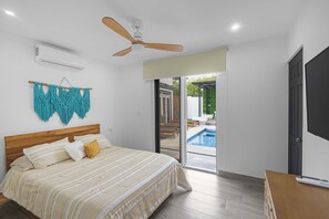 A bedroom with a bed, a ceiling fan, an air conditioning unit, and a view of a swimming pool through a glass door.
