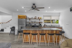 A modern kitchen with a central island, bar stools, a built-in oven, and a ceiling fan.