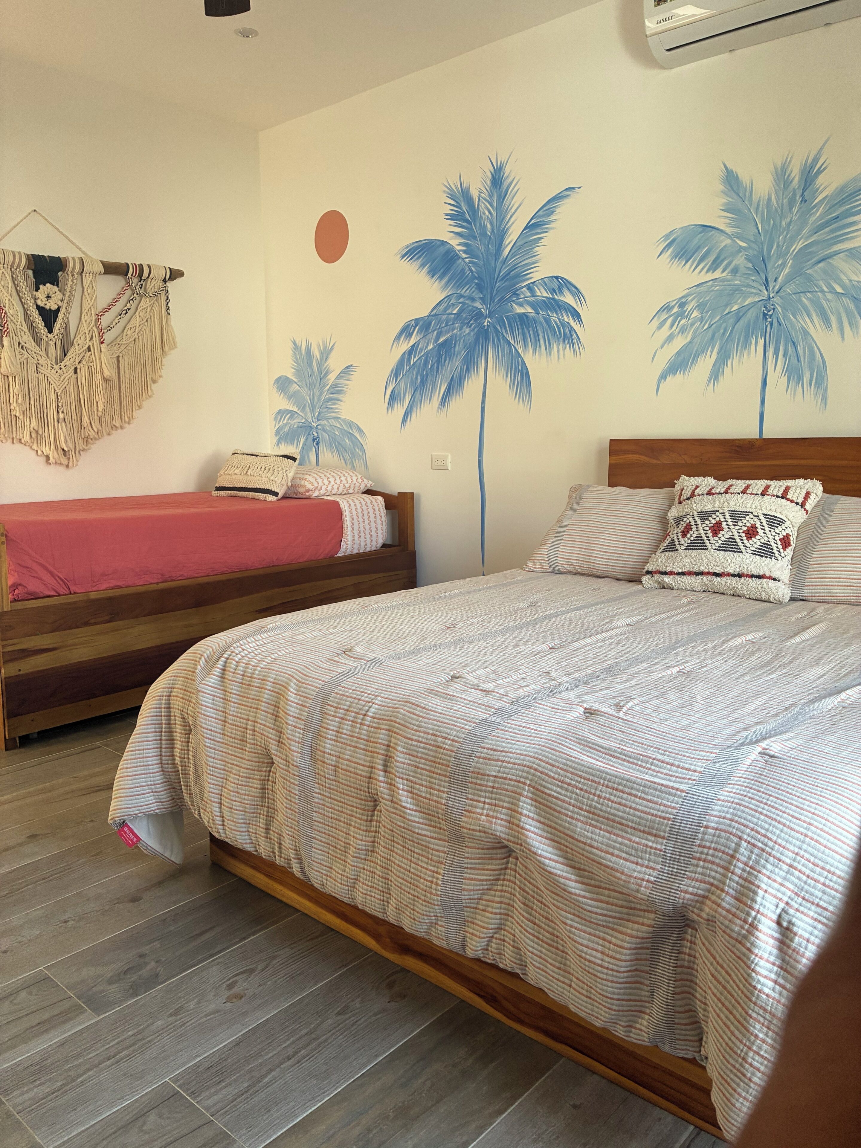 Un dormitorio con dos camas, un tapiz de macramé y decoración de palmeras.