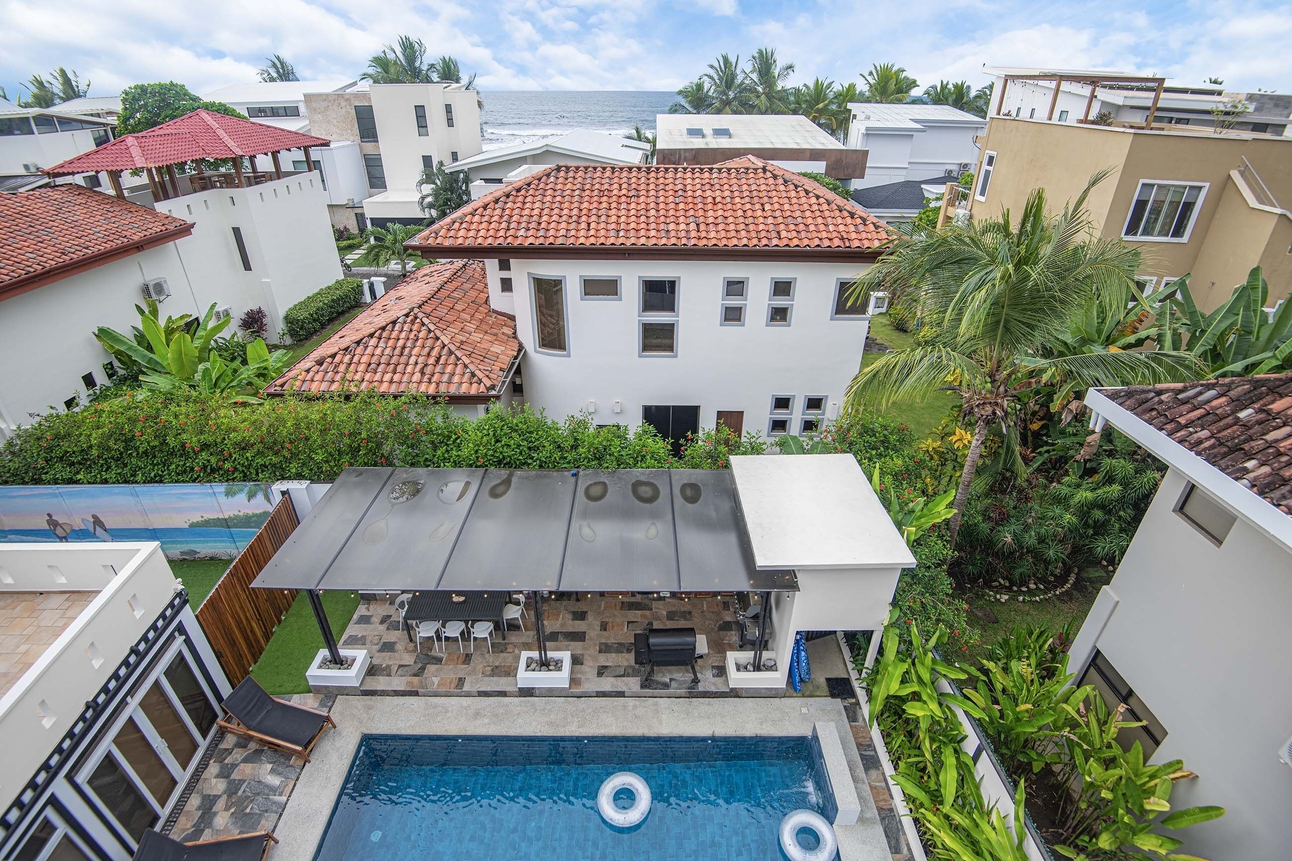A residential area with a swimming pool, patio with chairs and tables, and a view of the ocean.