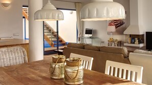 Un espace repas avec une table en bois, des chaises blanches et deux lampes suspendues.