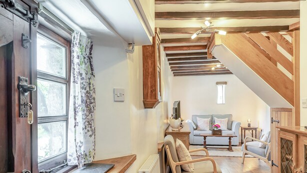 A cozy room with a wooden chair, a sofa, a table, and a staircase leading to another level. - 1 bedroom accommodation in Poundsgate, near Newton Abbot (Poundsgate, near Newton Abbot)