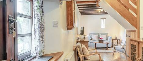 Una habitación acogedora con una silla de madera, un sofá, una mesa y una escalera que sube a otro nivel.