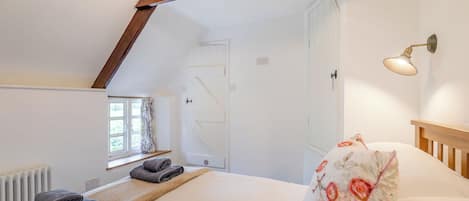 A bedroom with a sloped ceiling, a bed with a floral pillow, a bedside lamp, and a window with curtains.