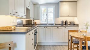 A modern kitchen with white cabinets, a built-in oven, a stove, and a sink. There is a window providing natural light and a dining table with chairs. - 1 bedroom accommodation in Poundsgate, near Newton Abbot (Poundsgate, near Newton Abbot)