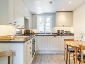 A modern kitchen with white cabinets, a built-in oven, a stove, and a sink. There is a window providing natural light and a dining table with chairs. - 1 bedroom accommodation in Poundsgate, near Newton Abbot (Poundsgate, near Newton Abbot)