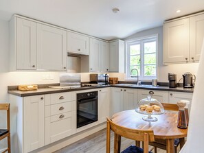 A modern kitchen with white cabinets, a built-in oven, and a dining area with a wooden table and chairs. - 1 bedroom accommodation in Poundsgate, near Newton Abbot (Poundsgate, near Newton Abbot)