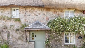 A stone building with a thatched roof, a green door, and a small porch area. - 1 bedroom accommodation in Poundsgate, near Newton Abbot (Poundsgate, near Newton Abbot)