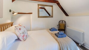 A bedroom with a wooden ceiling beam, a bed with white bedding, a chair, a radiator, and a mirror on the wall. - 1 bedroom accommodation in Poundsgate, near Newton Abbot (Poundsgate, near Newton Abbot)