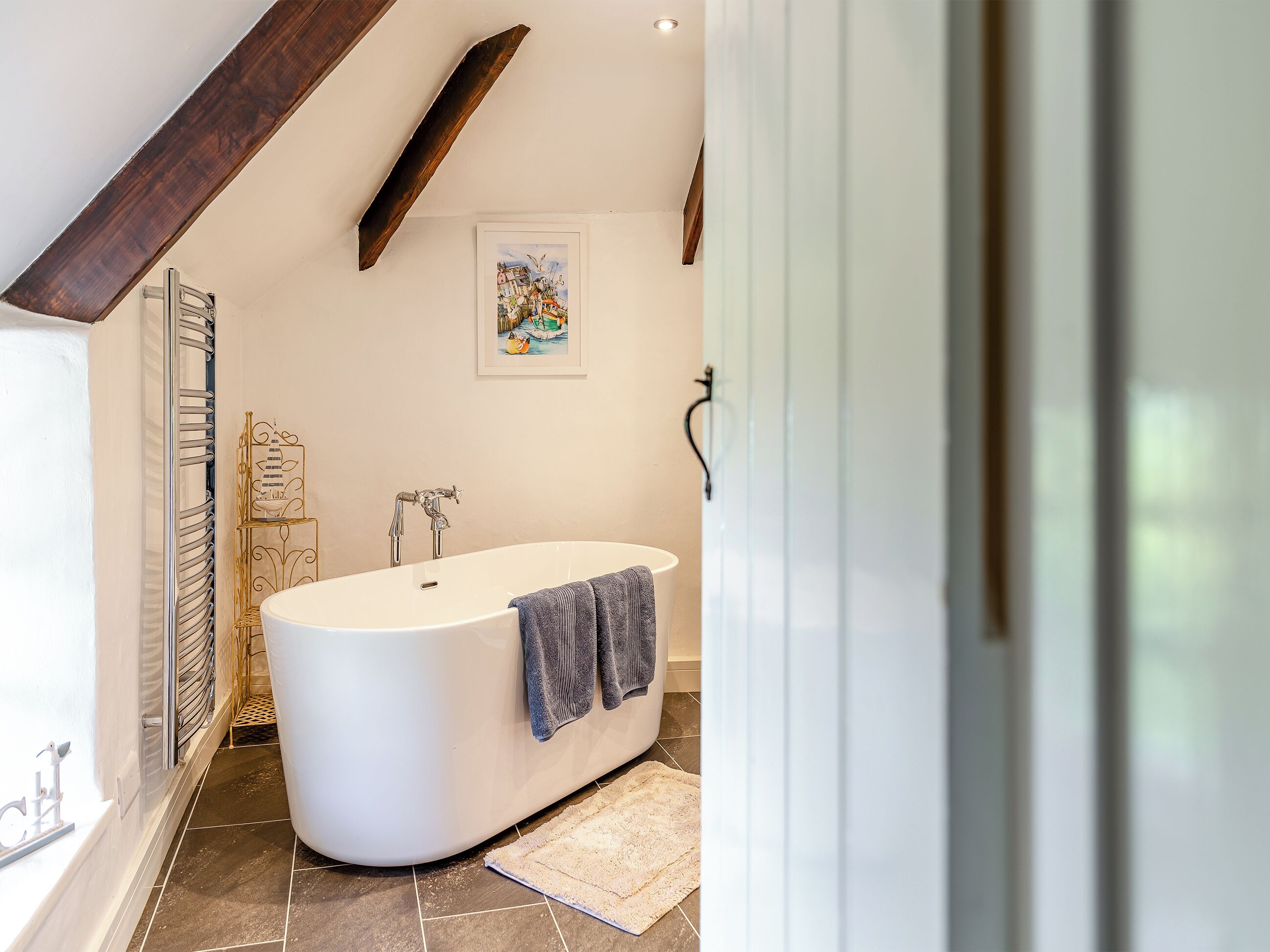A modern bathroom with a freestanding bathtub, a towel rack, and a framed artwork on the wall.