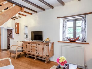 A cozy living room with a wooden cabinet, a flat-screen TV, a window with curtains, and a rustic chair.
