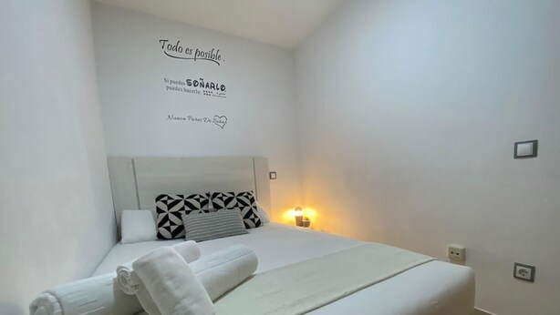 A neatly made bed with white linens and towels, geometric patterned pillows, and a wall with motivational text. - Madrid Delicias II - One-bedroom apartment (Madrid)