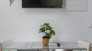 A modern dining area with a glass table, white chairs, a potted plant, and a mounted TV. - Madrid Pacífico - Nex to Retiro Park (Madrid)