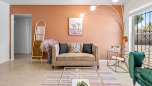 Un salon avec un canapé beige, un fauteuil vert, une table basse et un tableau accroché au mur.