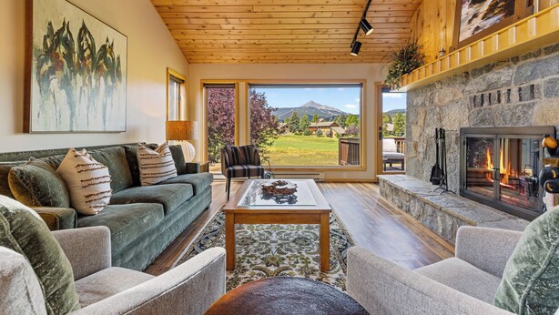 A cozy living room with a fireplace, comfortable seating, and a large window offering a scenic mountain view. - Lone Peak Lookout l Big Sky Golf Course (Big Sky)