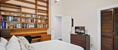 Un dormitorio con cama, escritorio, estantería, ventilador de techo, televisor y armario.