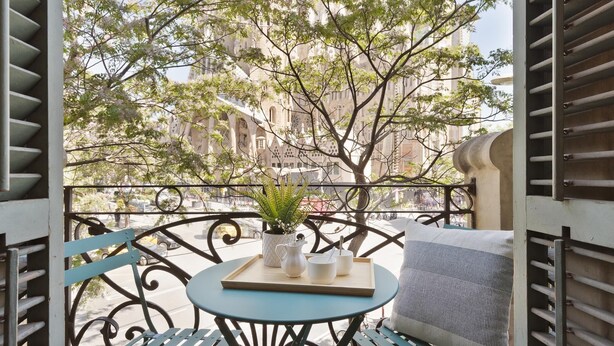 Un balcon offrant une vue sur la Sagrada Familia, avec une table agrémentée d’une plante, d’un plateau et d’un coussin.