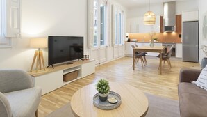 Un salon moderne doté d’un téléviseur à écran plat, d’une table basse agrémentée d’une plante et d’un coin repas illuminé par un lustre.