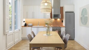 Une cuisine moderne avec des meubles blancs, une table à manger en bois et un luminaire suspendu.