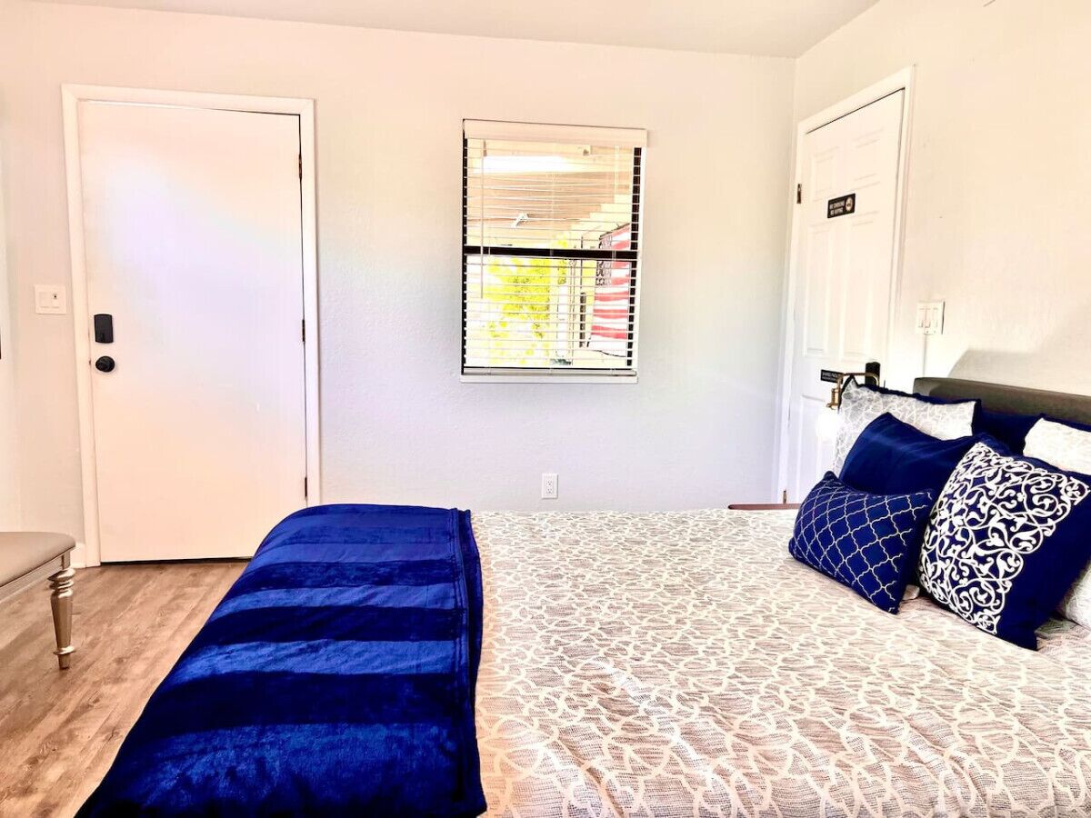 Un dormitorio con cama, un banco, una ventana con persianas y una puerta.