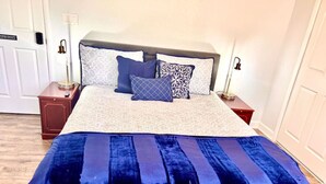 Un lit bien fait, avec une couverture bleue et des oreillers, une table de chevet avec une lampe, et une porte portant l’inscription « Espace à usage partagé ».