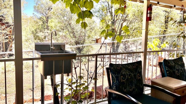 Une terrasse couverte avec un barbecue, des sièges d’extérieur et une vue sur les arbres et une clôture.