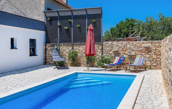 Relax by the serene pool surrounded by a natural stone wall and shaded by a red umbrella.