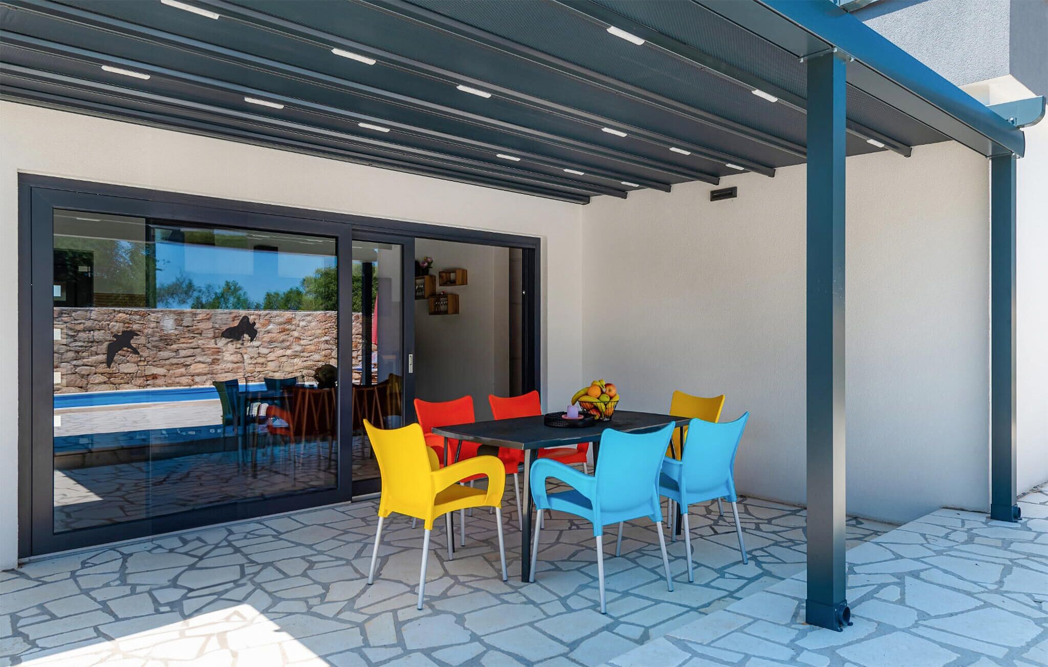 An outdoor patio with a table and chairs, a stone wall, and a glass door leading to a pool area.
