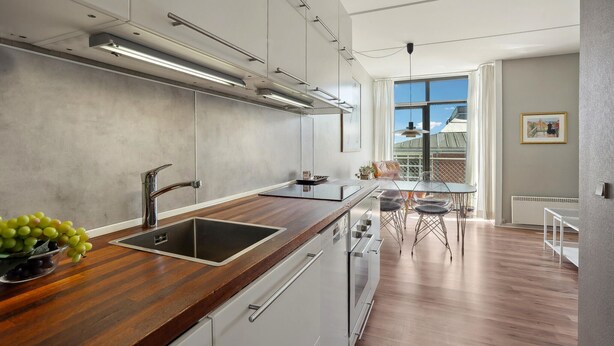 Une cuisine moderne dotée d’un plan de travail en bois, d’un évier en acier inoxydable et de meubles blancs.