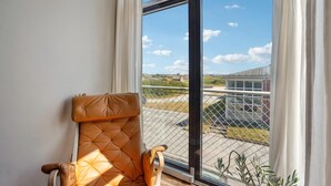 Une pièce dotée d’une grande fenêtre, d’un fauteuil confortable et offrant une vue sur un bâtiment et la verdure environnante.