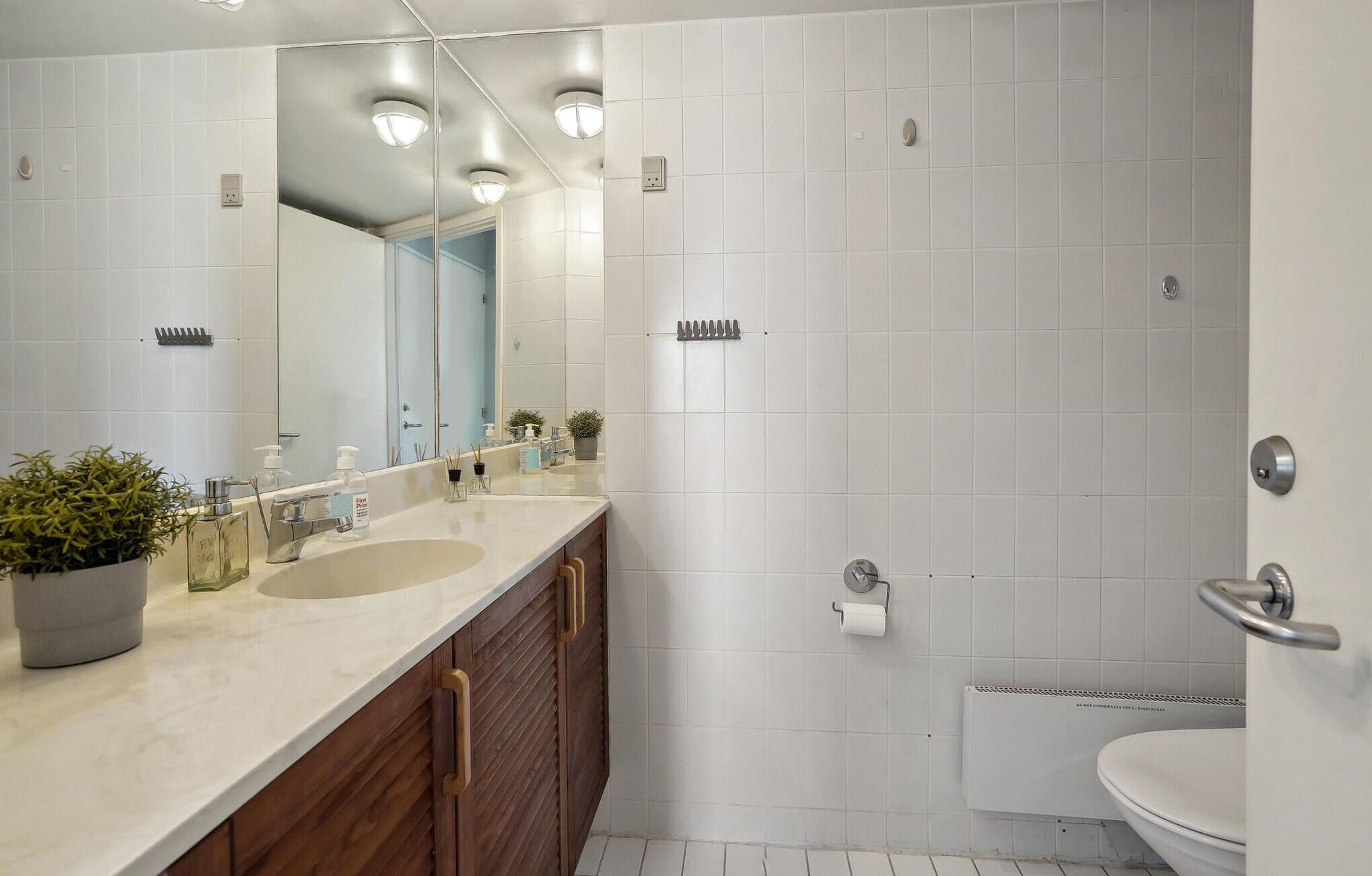 A modern bathroom with a large mirror, two sinks, a toilet, and a shower area.