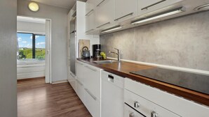 Une cuisine moderne avec des armoires blanches, un plan de travail en bois, un lave-vaisselle encastré et une vue sur la verdure à l’extérieur.