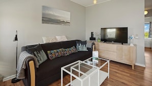Un salon moderne avec un canapé, une table basse en verre, un téléviseur à écran plat et un tableau accroché au mur.