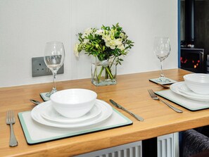 Ein Esstisch ist gedeckt mit weißen Tellern, Schüsseln, Besteck und Gläsern, dazu steht ein Blumenstrauß auf dem Tisch.