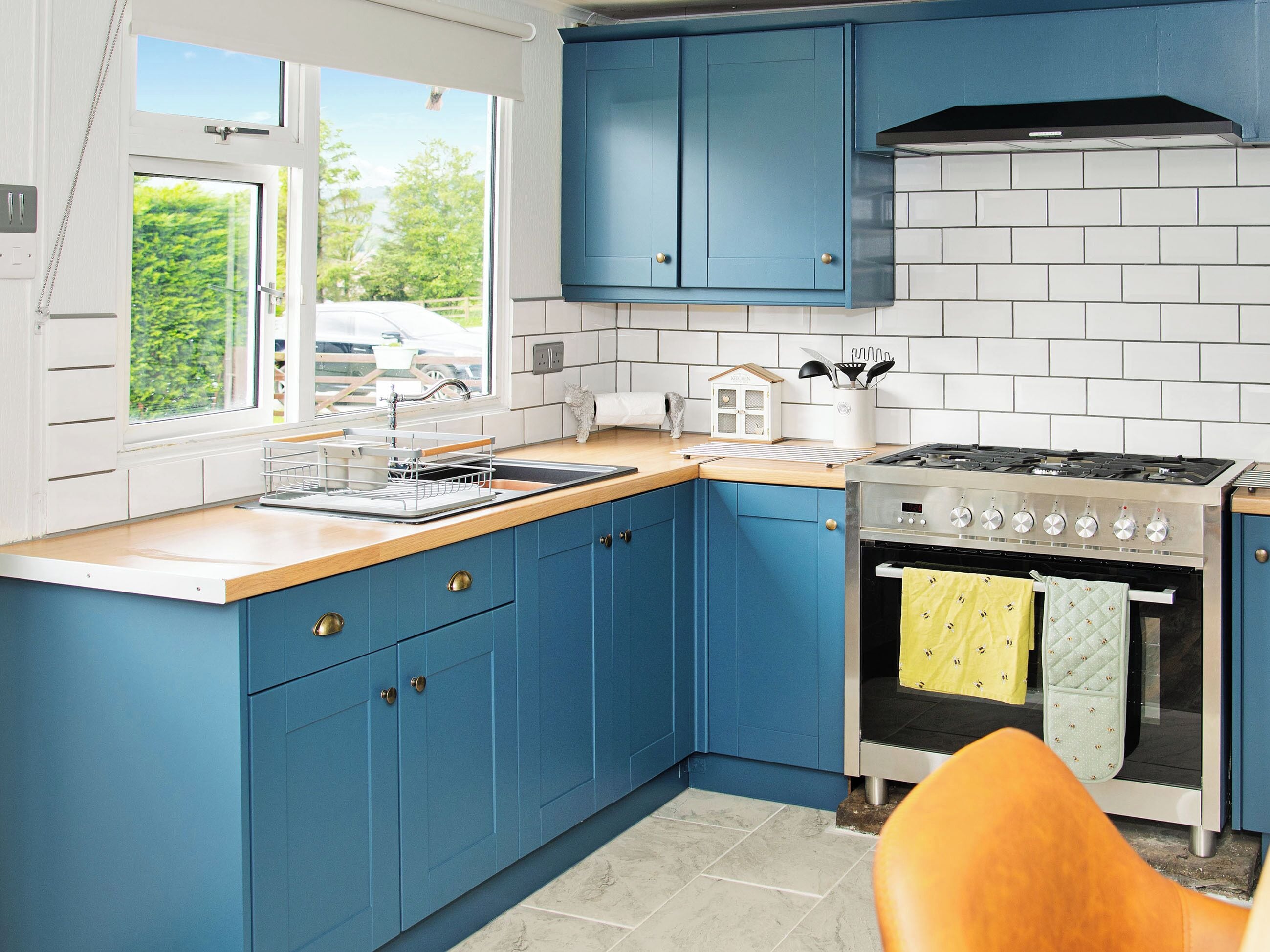 A kitchen with blue cabinets, a stove, and a window with a view of greenery.