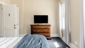 Una camera da letto con un letto, una cassettiera in legno, una televisione e una porta.
