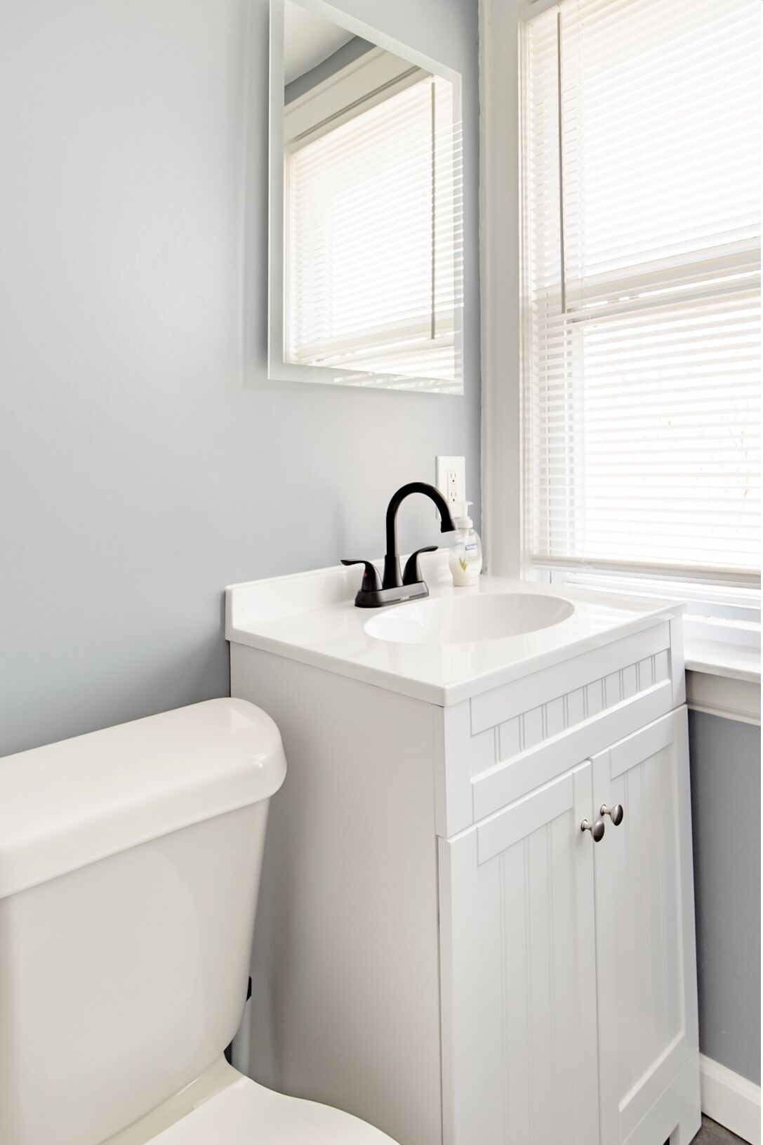 A bathroom with a white toilet, a white sink with a black faucet, and a mirror above the sink.