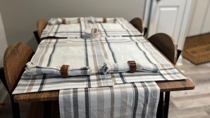 Une table à manger recouverte d’une nappe à carreaux, des chaises en bois et, au fond, une porte blanche.
