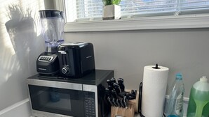 Un plan de travail de cuisine avec un four à micro-ondes, un mixeur, un grille-pain, un bloc à couteaux, un rouleau d’essuie-tout et des produits de nettoyage.
