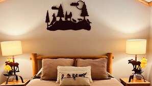 Un dormitorio con cama, dos mesitas de noche, lámparas y un adorno en la pared.