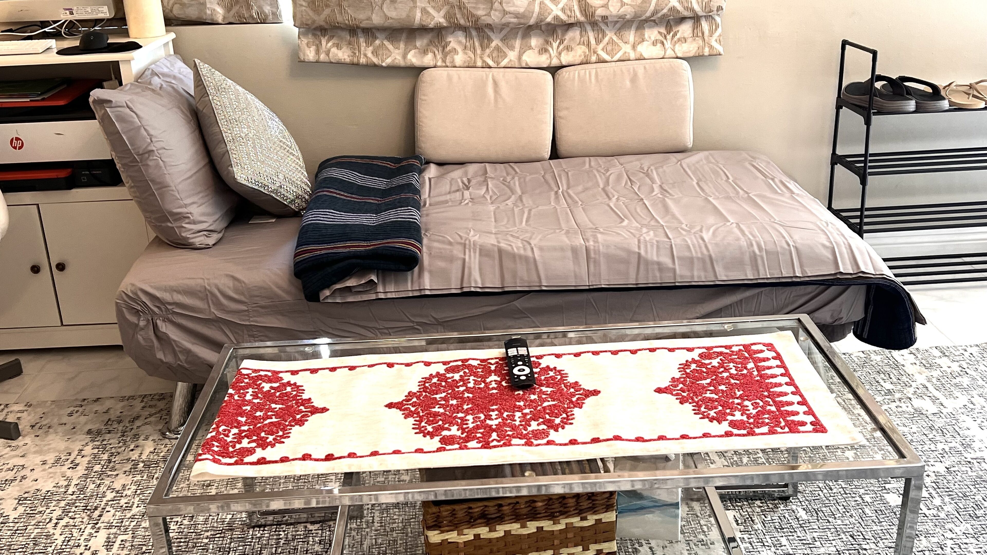 Een netjes ingerichte slaapkamer met een bed, een glazen salontafel met een tafelkleed met een rood-wit patroon, en een klein nachtkastje.